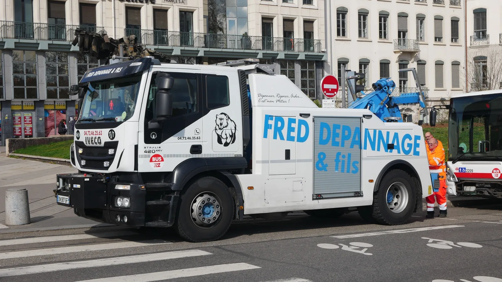 Witte Franse takelwagen van een bergingsbedrijf in een stad, met een medewerker in oranje hesje