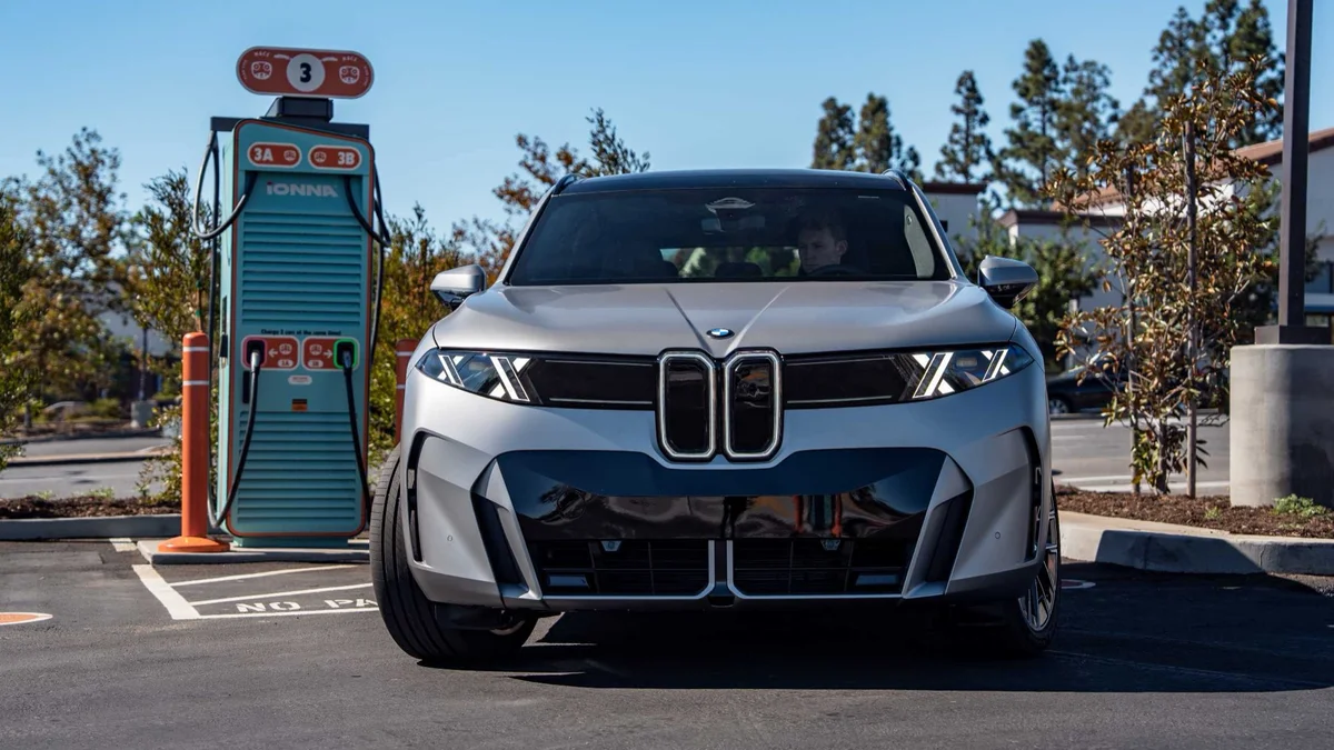 Zilvergrijze BMW iX5 van voren bij een snellader van IONNA op een zonnige parkeerplaats