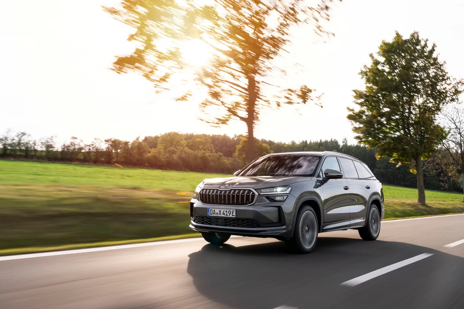 Grijze Škoda Kodiaq rijdend op een landweg, van schuin voren in tegenlicht