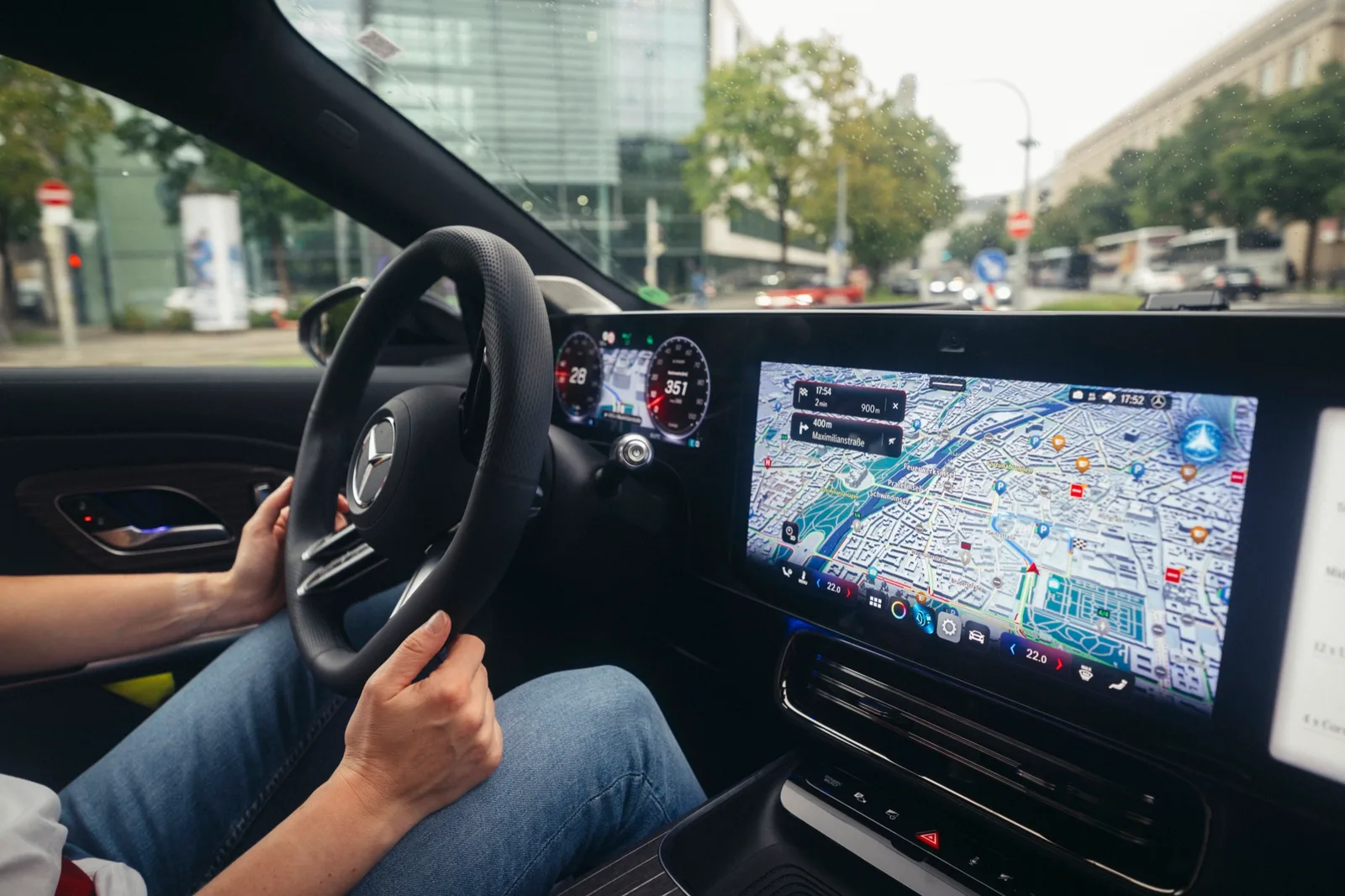 Handen aan het stuur van een Mercedes met de navigatiekaart op het scherm