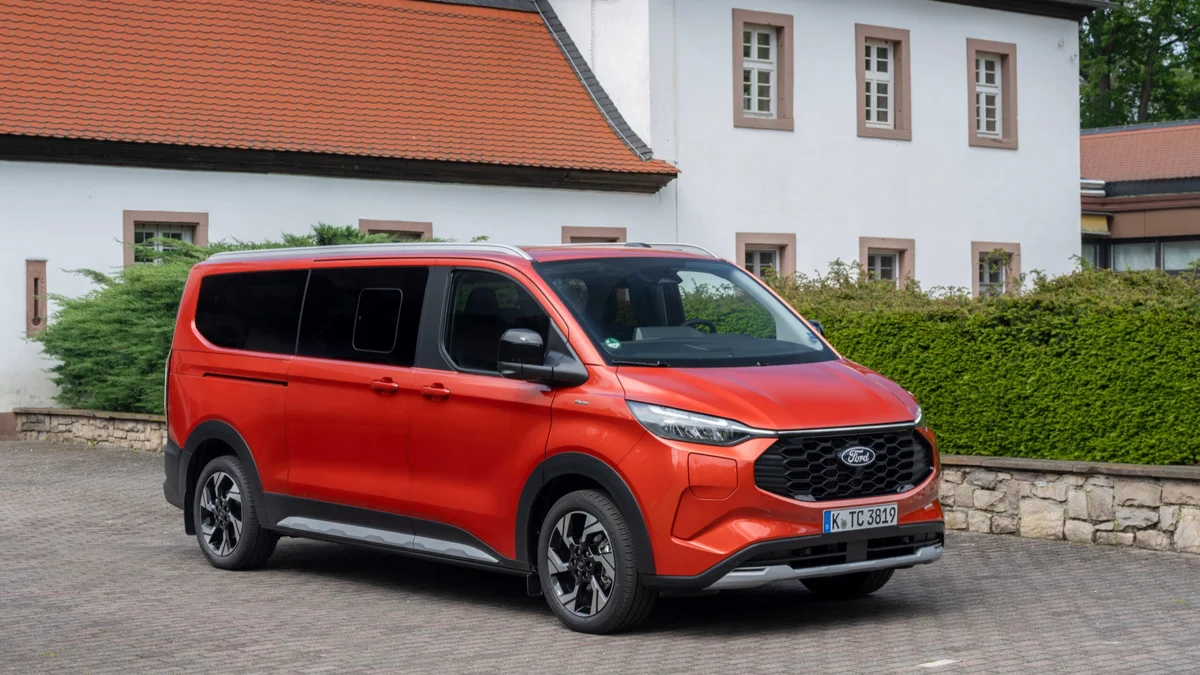 Rode Ford Tourneo Custom Active van schuin voren, geparkeerd op kinderkopjes voor een wit gebouw