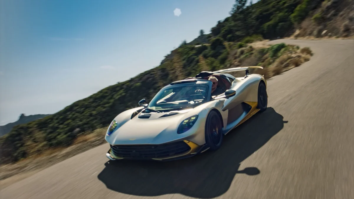 Zilvergrijze Aston Martin Valhalla Spider zonder dak rijdend over een bergweg, van schuin voren